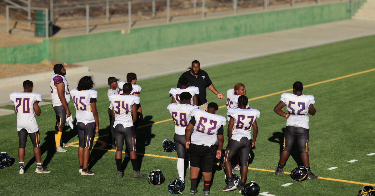High school football team preparing on the field with coach guidance.