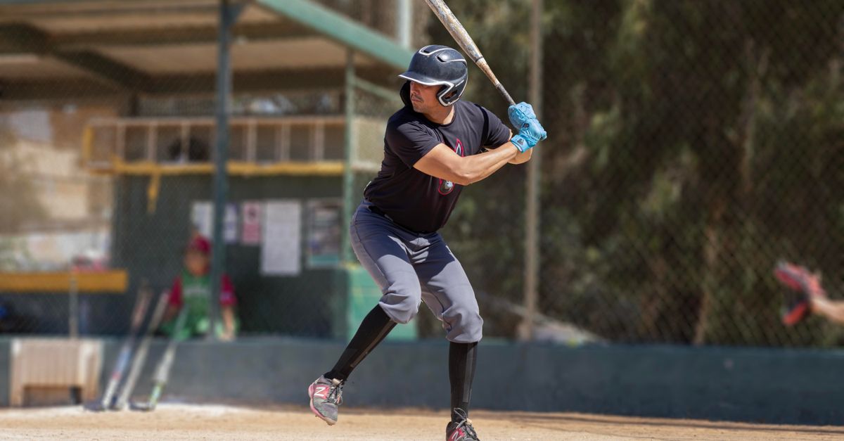 A baseball player in action at a sunlit outdoor baseball field, preparing to swing.
